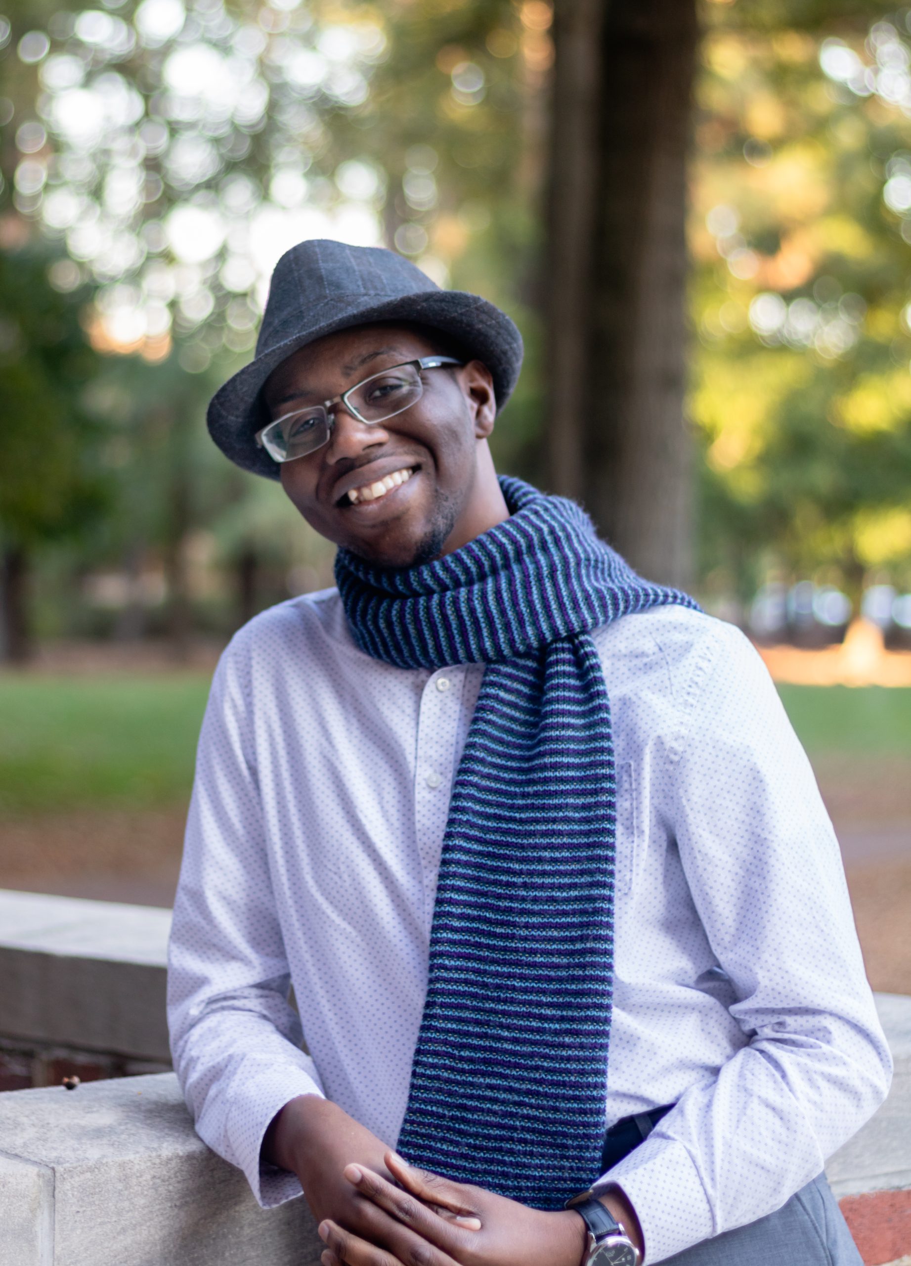 Image of man with hat and scarf leaning on the edge of a ledge candidly looking into the camera 